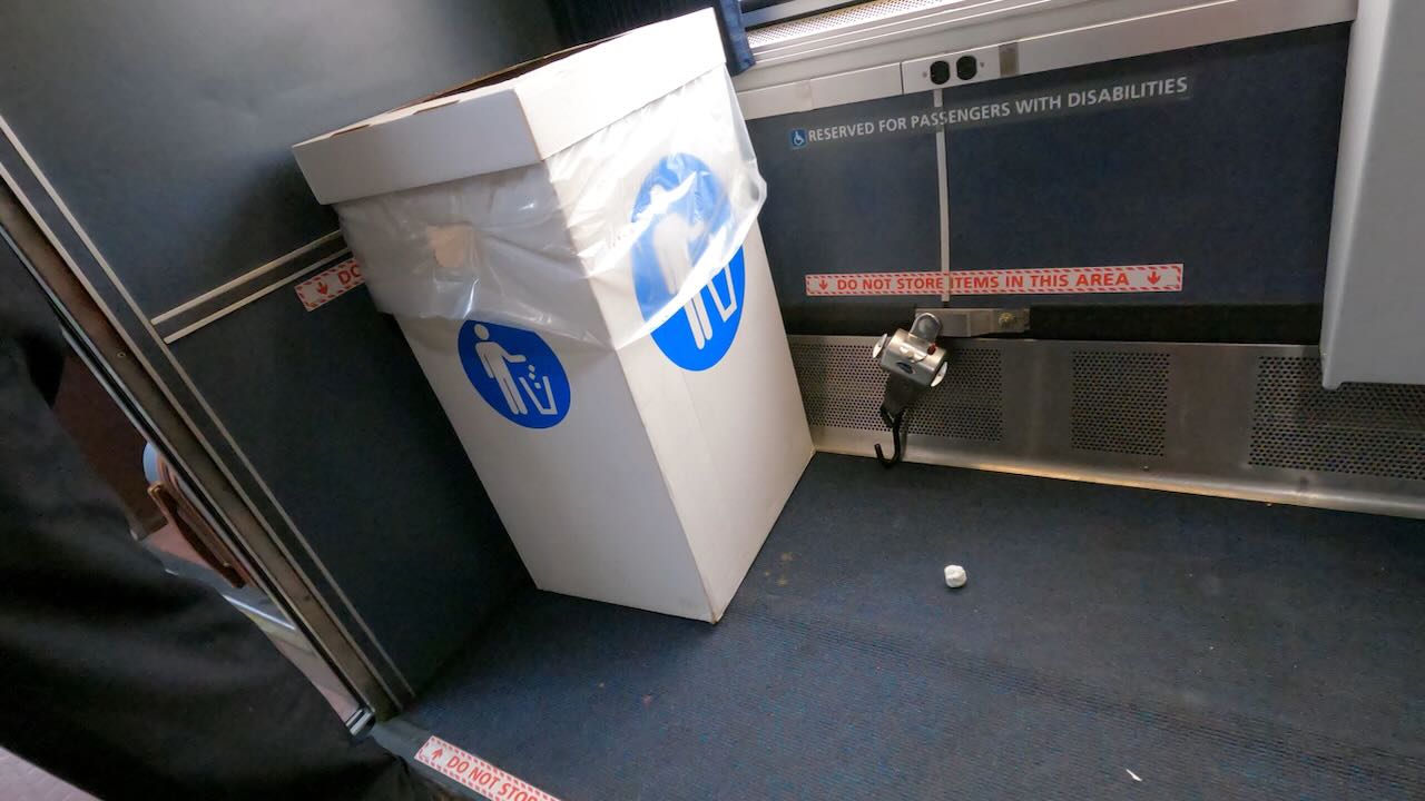 A large trash can blocks one of three signs that say, DO NOT STORE ITEMS IN THIS AREA. A sign on the wall says, ♿ RESERVED FOR PASSENGERS WITH DISABILITIES. An escapee ball of trash sits on the floor.